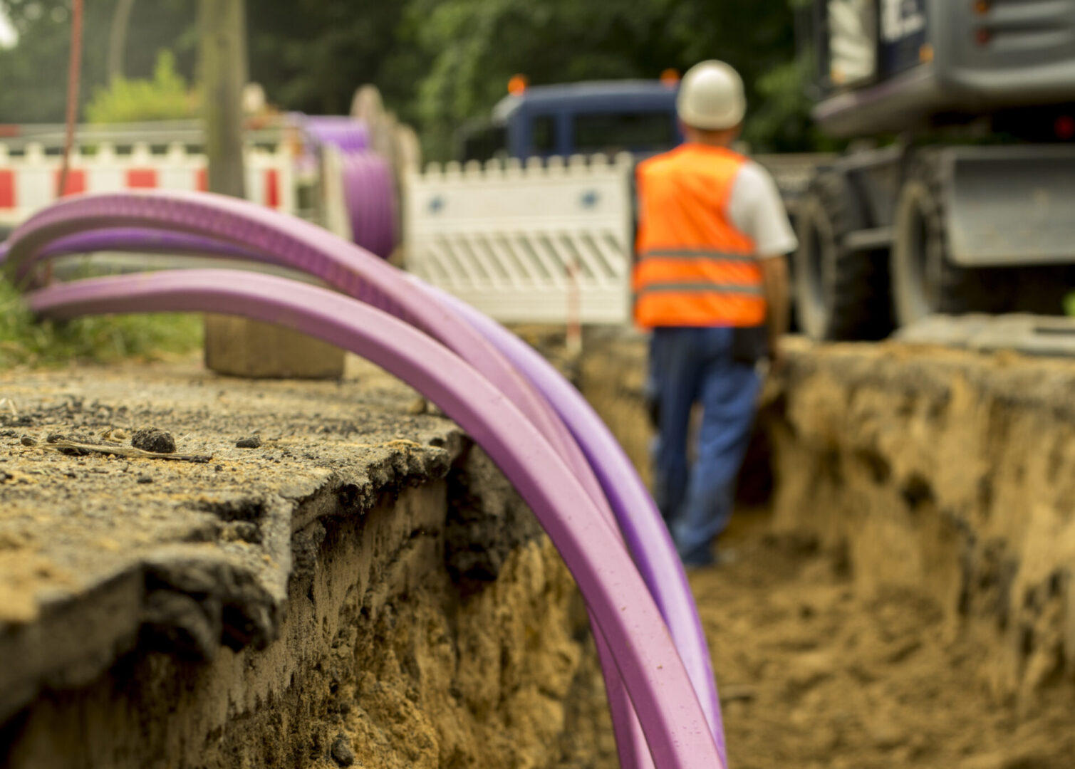 Purple conduit in a trench, worker blurred.